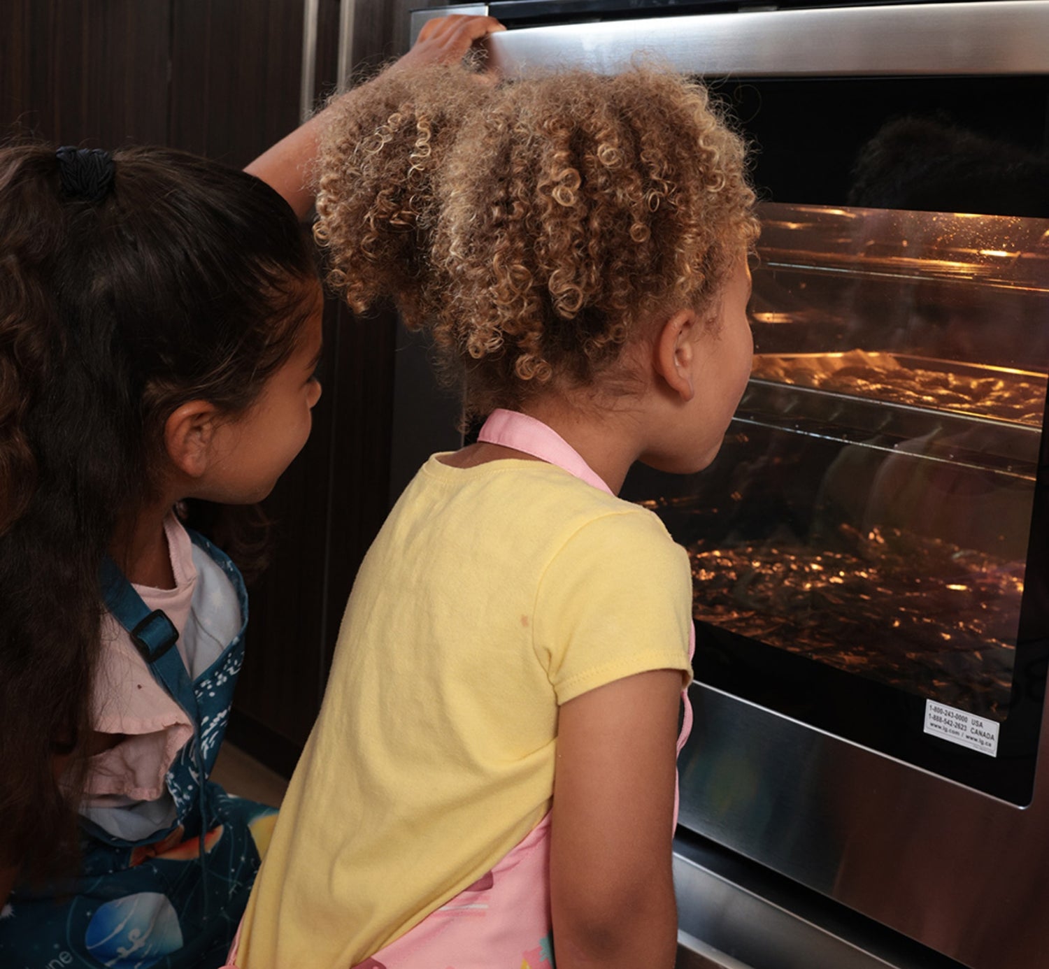 two children watching cookies bake in the oven